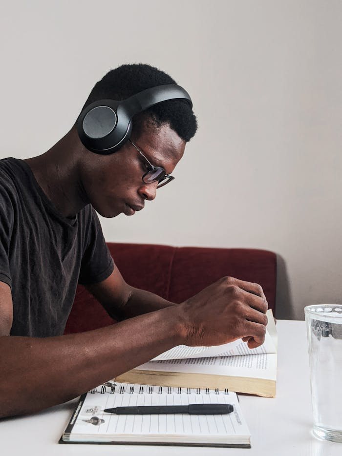pexels-photo-3466163 An adult man intensely studying with headphones, pen, and notebook at a desk indoors.