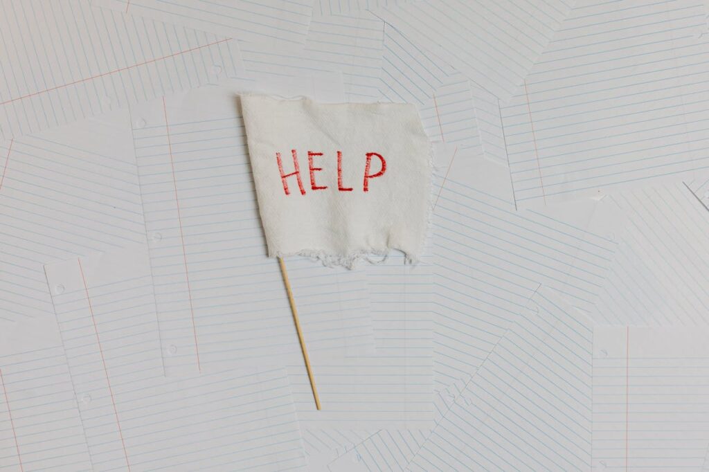 pexels-photo-8386732 A fabric flag with 'HELP' on a scattered notepaper background, symbolizing distress or overwhelm.